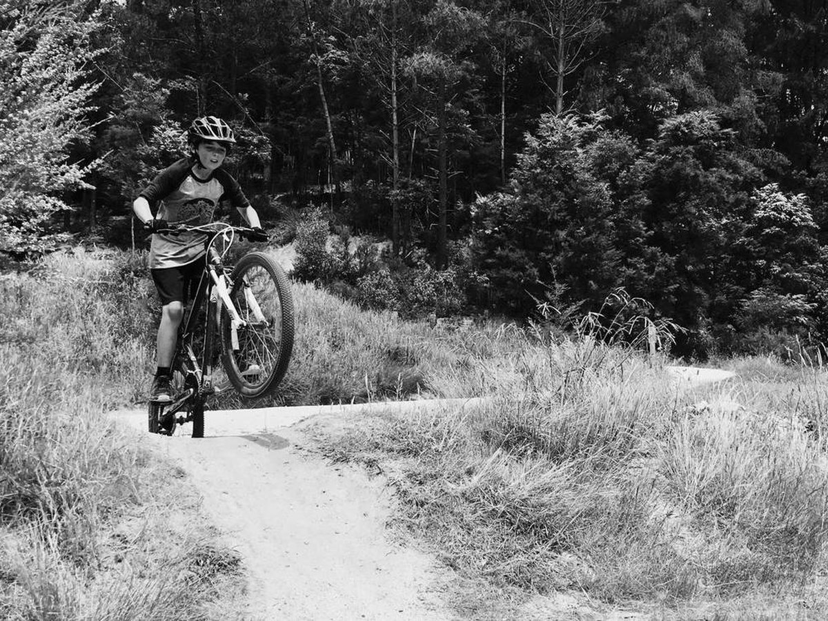 A 24-inch kids mountain bike in a driveway, stand-over already checked. A lid waits on the bar.